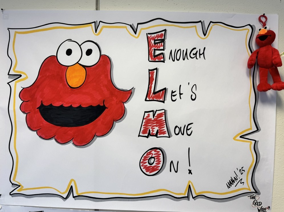 Flipover met een getekende Elmo naast de letters E, L, M en O, uitgeschreven als Enough, Let's Move On. Aan de rand van het vel hangt een Elmo-knuffel.